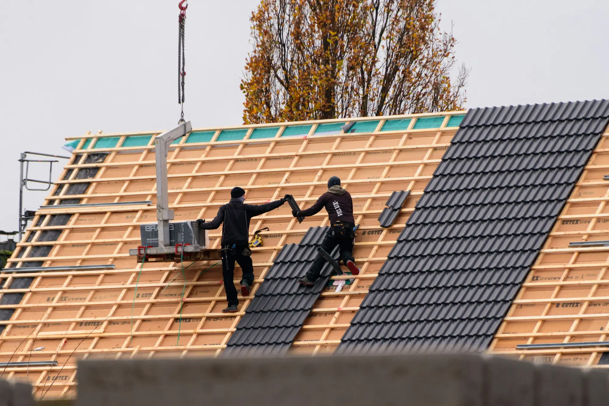 Dachdecker verlegen anthrazitfarbene Dachziegel auf einem Neubau